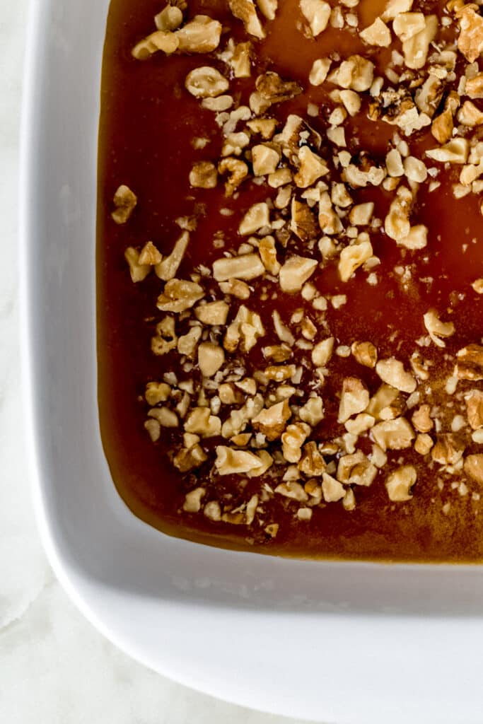 mixture for sticky buns in white baking dish topped with chopped walnuts
