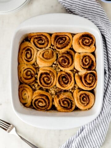 baked sticky buns in white baking dish with striped napkin, fork, and white plates