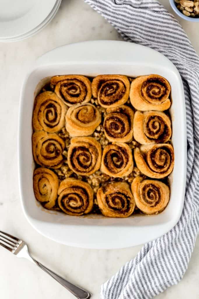 baked sticky buns in white baking dish with striped napkin, fork, and white plates