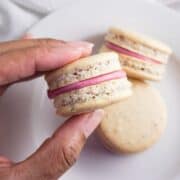 Hand holding a macaron over a plate.