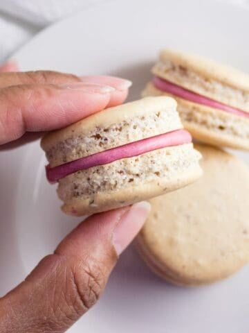 Hand holding a macaron over a plate.