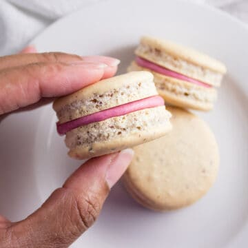 Hand holding macaron over plate.