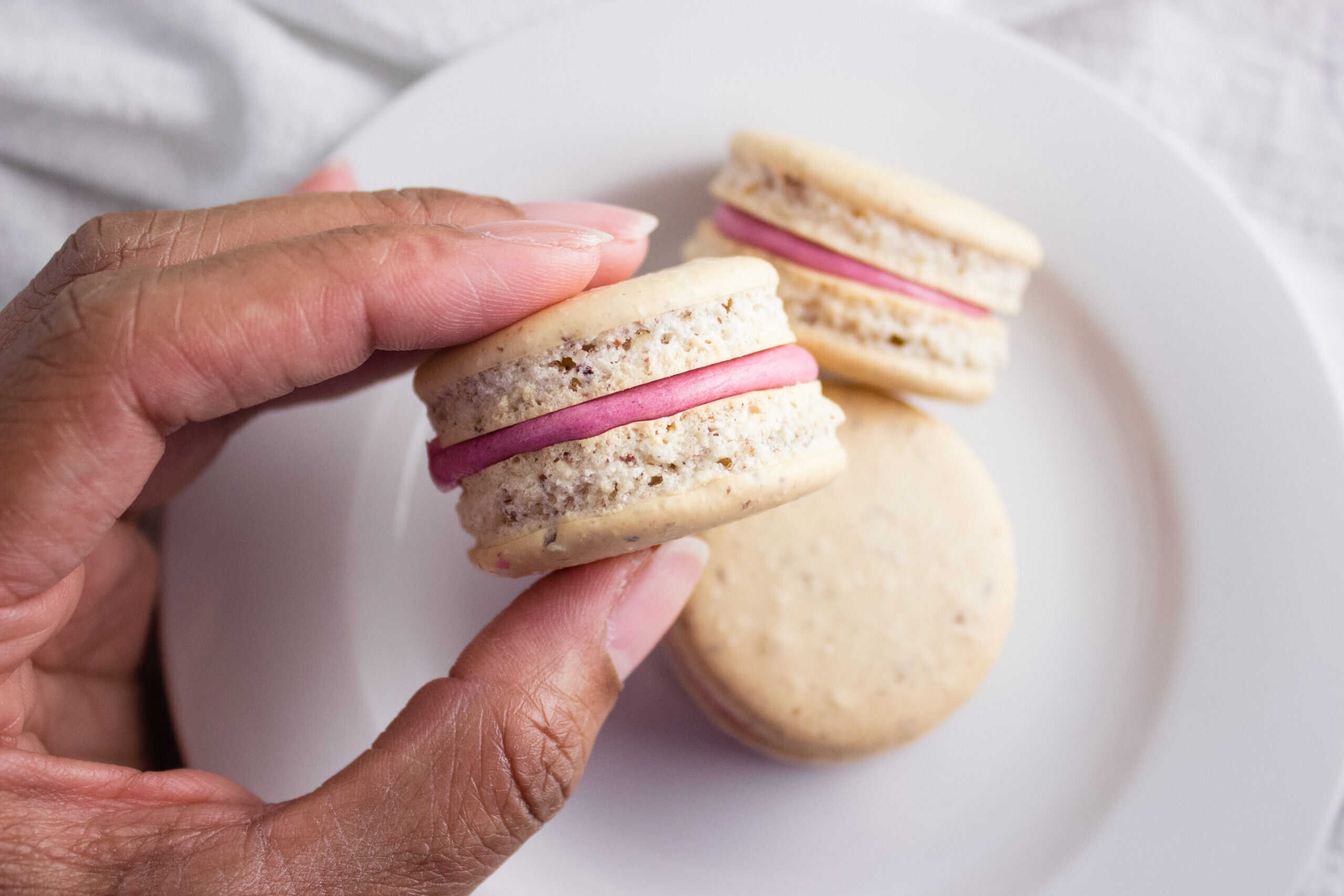Hand holding macaron over plate. 