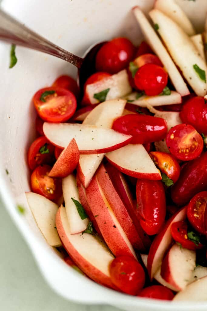 ingredients for tomato peach salad in white mixing bowl with spoon 