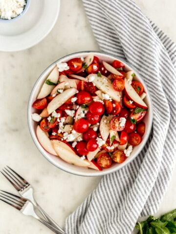 overhead view tomato peach salad in large serving bowl with forks, plates, and cloth napkin