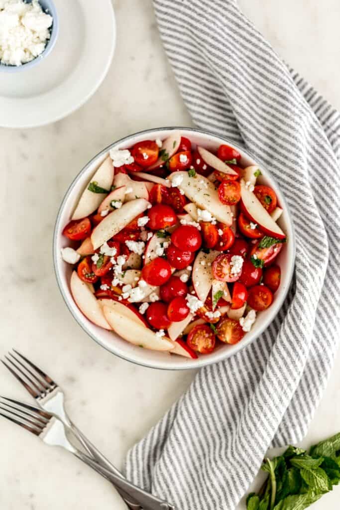 overhead view tomato peach salad in large serving bowl with forks, plates, and cloth napkin 