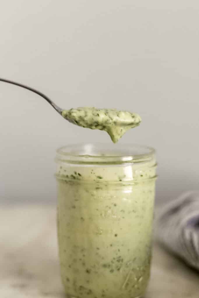 hand holding spoon with cilantro lime dressing over glass jar 