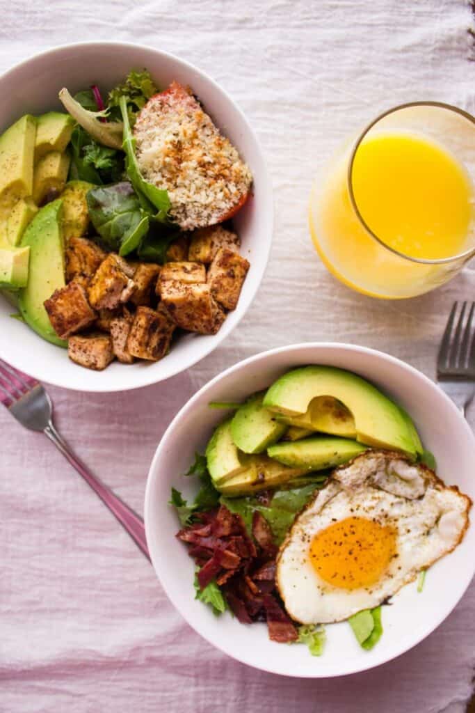 overhead view of two breakfast bowls with forks and glass of orange juice