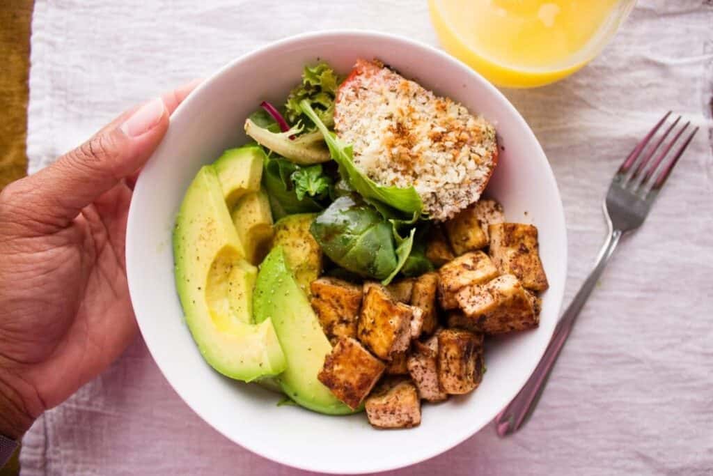 overhead view of breakfast bowls with hand, fork, and glass of juice