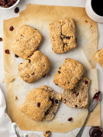 overhead view of baked scones on parchment paper with dried cranberries and a knife with jam on it.