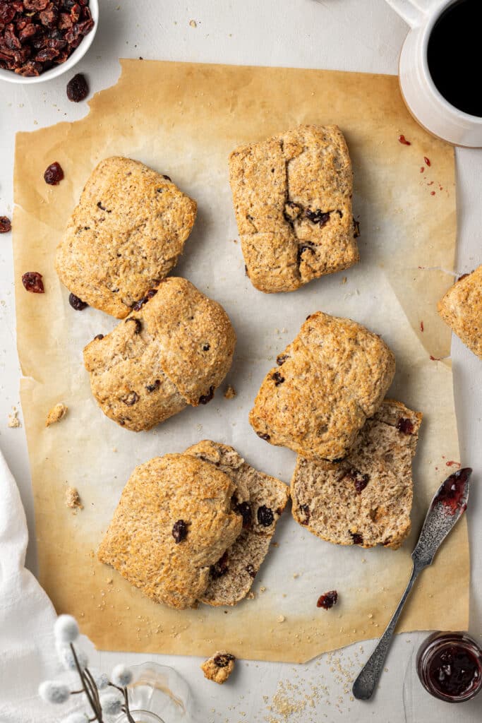 overhead view of baked scones on parchment paper with dried cranberries and a knife with jam on it.