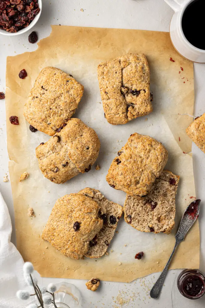 overhead view of baked scones on parchment paper with dried cranberries and a knife with jam on it.