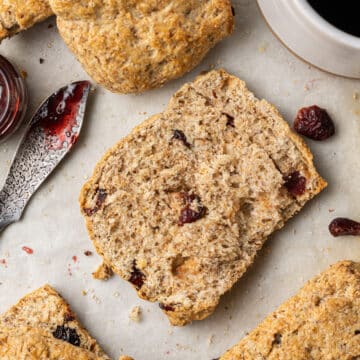 half of flaxseed scone with others around it with spreader and jam.