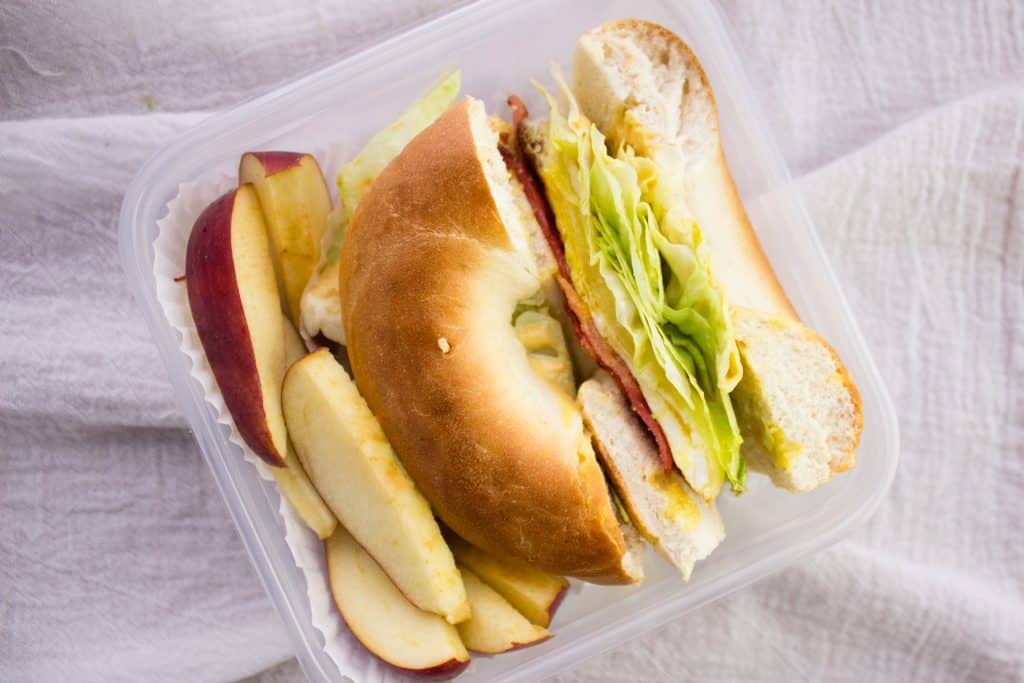 overhead view of bagel sandwich and apple slices in container