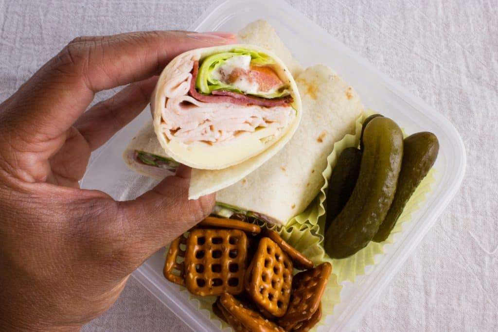 hand holding lunch wrap over the rest of the lunch in a container