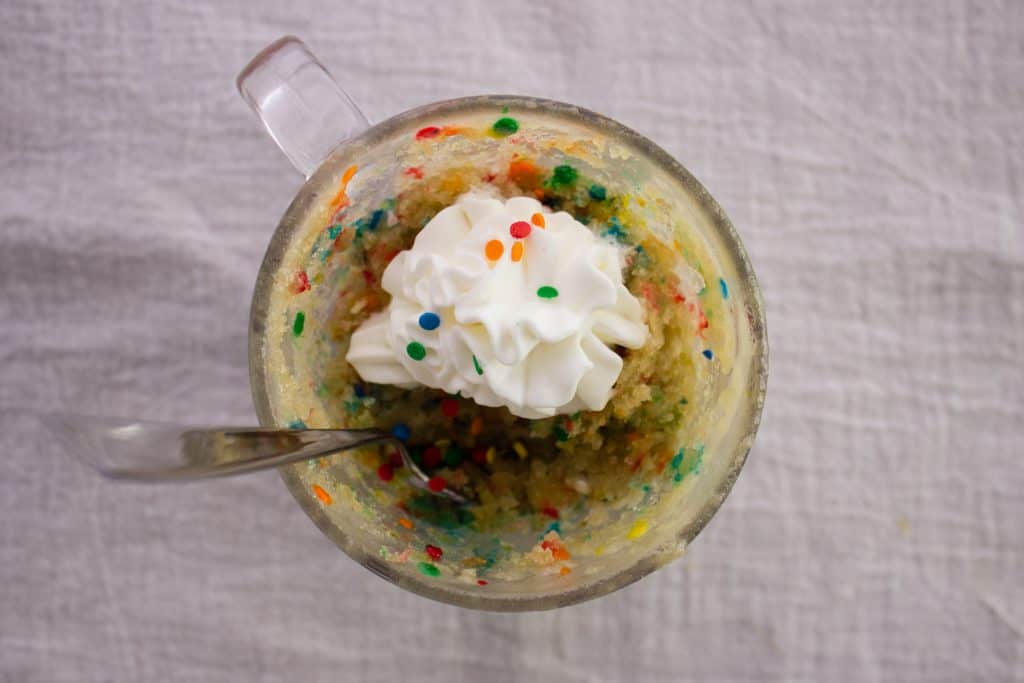 overhead view of mug cake topped with whipped cream with a spoon in it