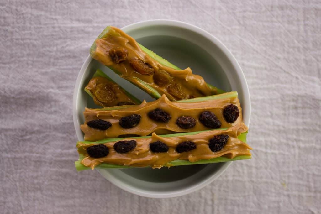 celery sticks topped with peanut butter and raisins in white bowl 
