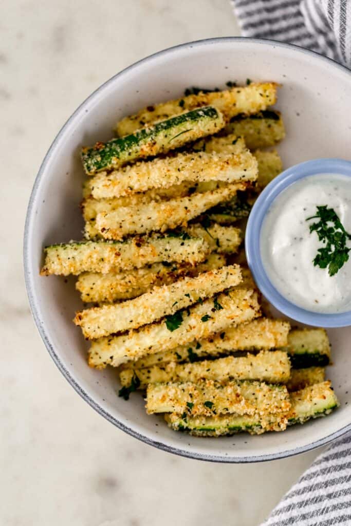 overhead view zucchini fries in serving bowl with small bowl of dipping sauce and cloth napkin