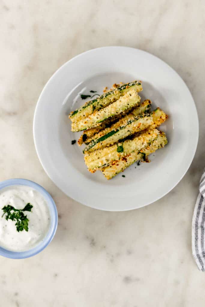 small white plate with baked zucchini fries on it next to small bowl with dipping sauce 