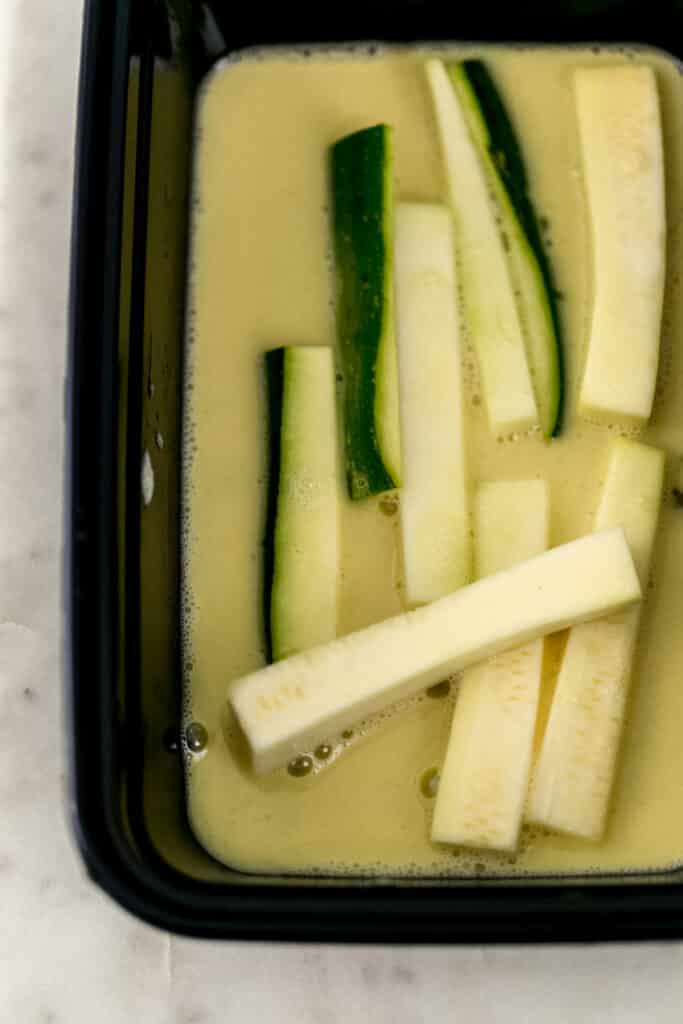 zucchini fries in container with egg mixture 