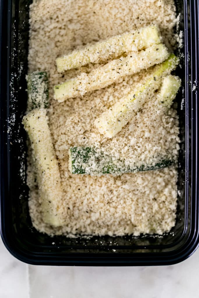 zucchini fries in container with breadcrumb mixture 
