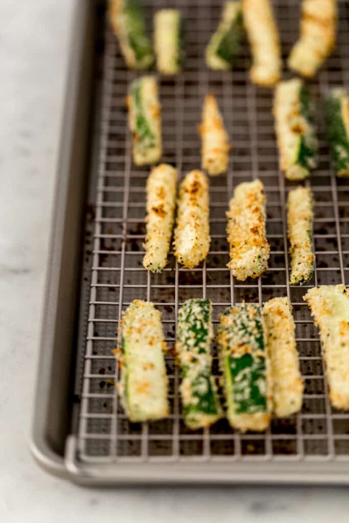 close up view baked zucchini fries on baking sheet with rack