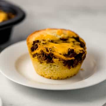 close up side view of single muffin on white plate with more in muffin pan in the background