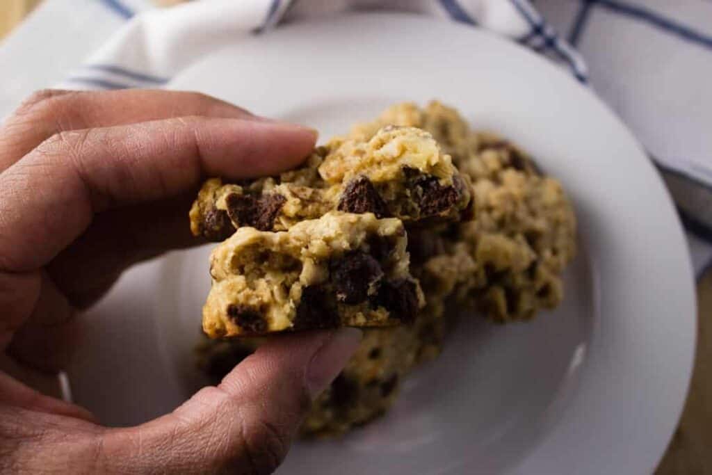 Chocolate Chip Tahini Cookies being held by hand over white plate