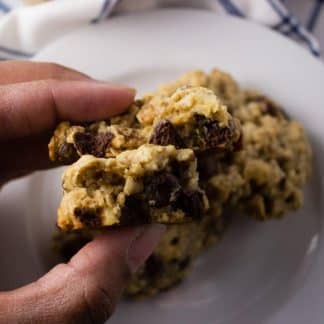 Close-up view Chocolate Chip Tahini Cookies on white plate with hand holding it.