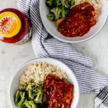 overhead view two bowls of food with pork chops, rice, and broccoli with napkin, forks, and jar of salsa