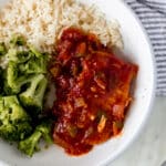 overhead view of shallow bowl of peachy salsa pork chops, rice, and broccoli with napkin