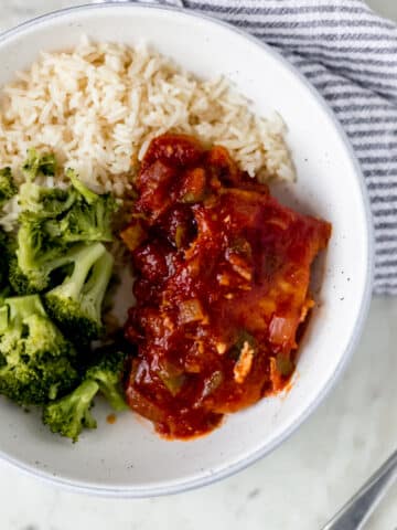 overhead view of shallow bowl of peachy salsa pork chops, rice, and broccoli with napkin