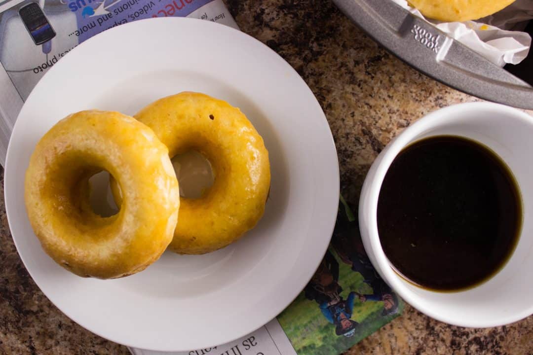 overhead view of two doughnuts on white plate beside a cup of coffee