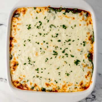 baked lasagna in white square baking dish on marble surface