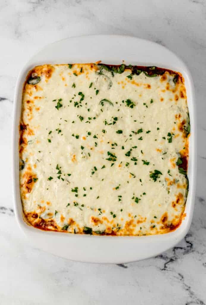 baked lasagna in white square baking dish on marble surface