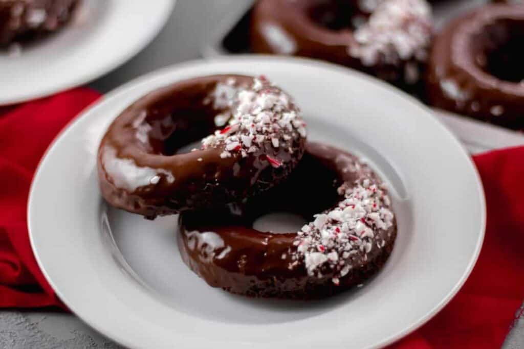 Close-up side view of two Chocolate Peppermint Doughnuts on a white plate over red napkin 