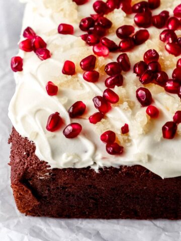 Close up side view of finished gingerbread cake topped with frosting on parchment paper.