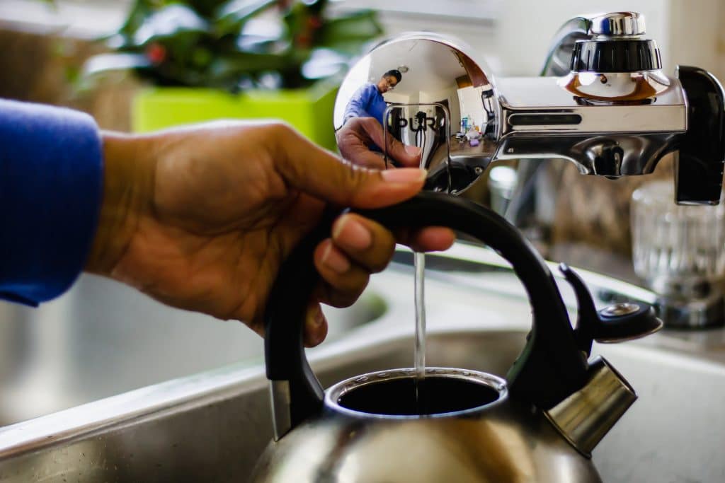 close-up side view of hand holding kettle under running water