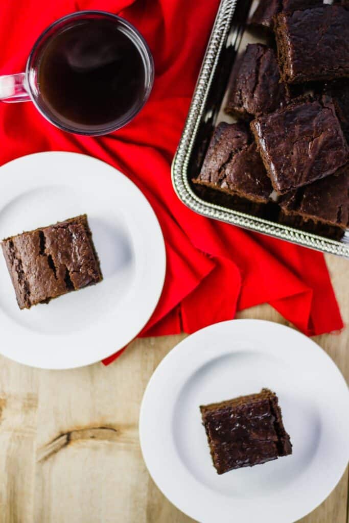 Overhead view of Ginger Cake Squares on white plates, silver platter, over a red napkin with a cup of coffee