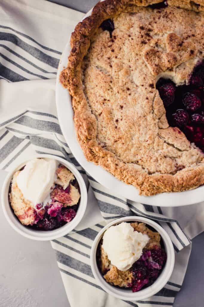 Overhead view Blackberry Cobbler in baking dish and two bowls over napkin