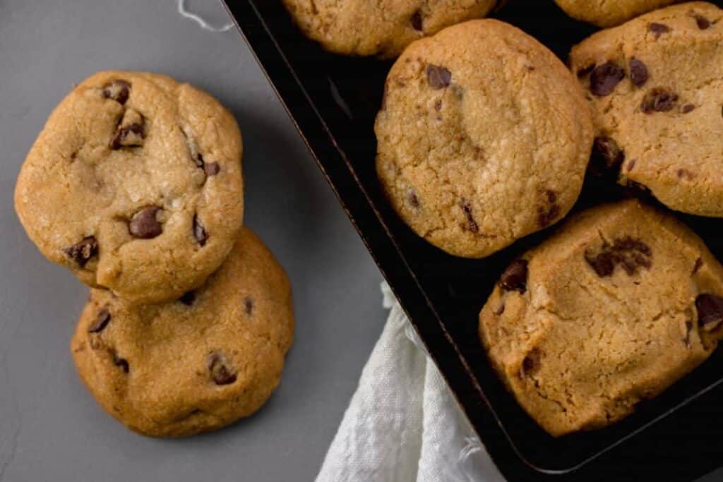 Overhead view of two Coconut Oil Chocolate Chip Cookies next to more on a sheet pan 