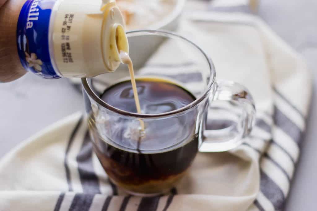 side view of creamer being added to a cup of coffee