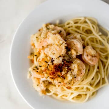 overhead view baked shrimp scampi over pasta on white plate