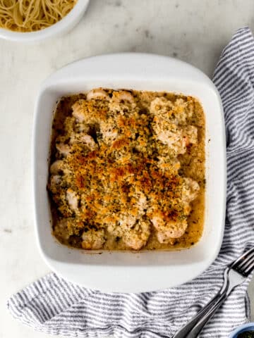 white baking dish with baked shrimp scampi by napkin and forks