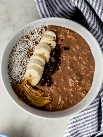 chocolate mocha overnight oats in white bowl topped with banana slices, coconut, peanut butter, and chocolate