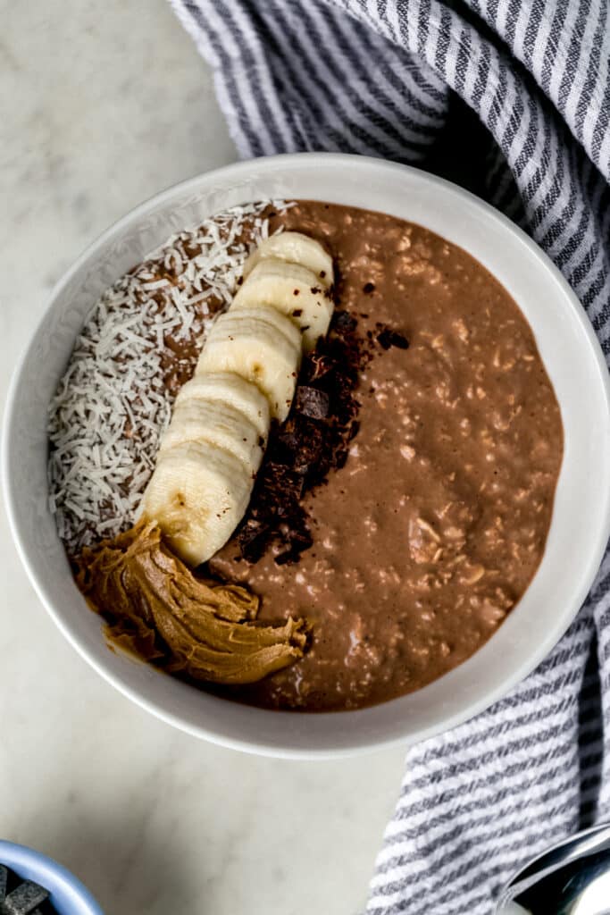 chocolate mocha overnight oats in white bowl topped with banana slices, coconut, peanut butter, and chocolate