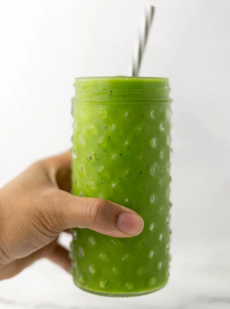hand holding glass with straw and smoothie in it. 
