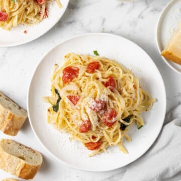overhead view of pasta on two white plates next to bread and a glass of white wine.