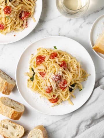 overhead view of pasta on two white plates next to bread and a glass of white wine.