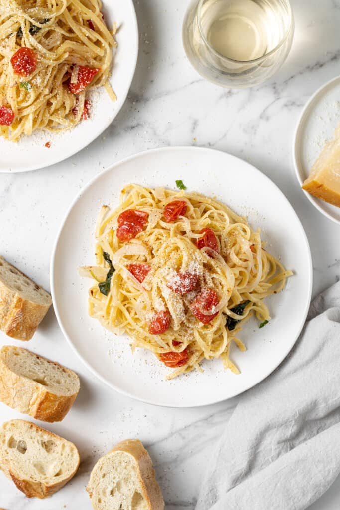 overhead view of pasta on two white plates next to bread and a glass of white wine.